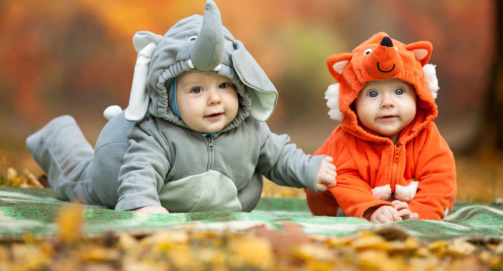 Two babies dressed in costumes sitting on the ground.