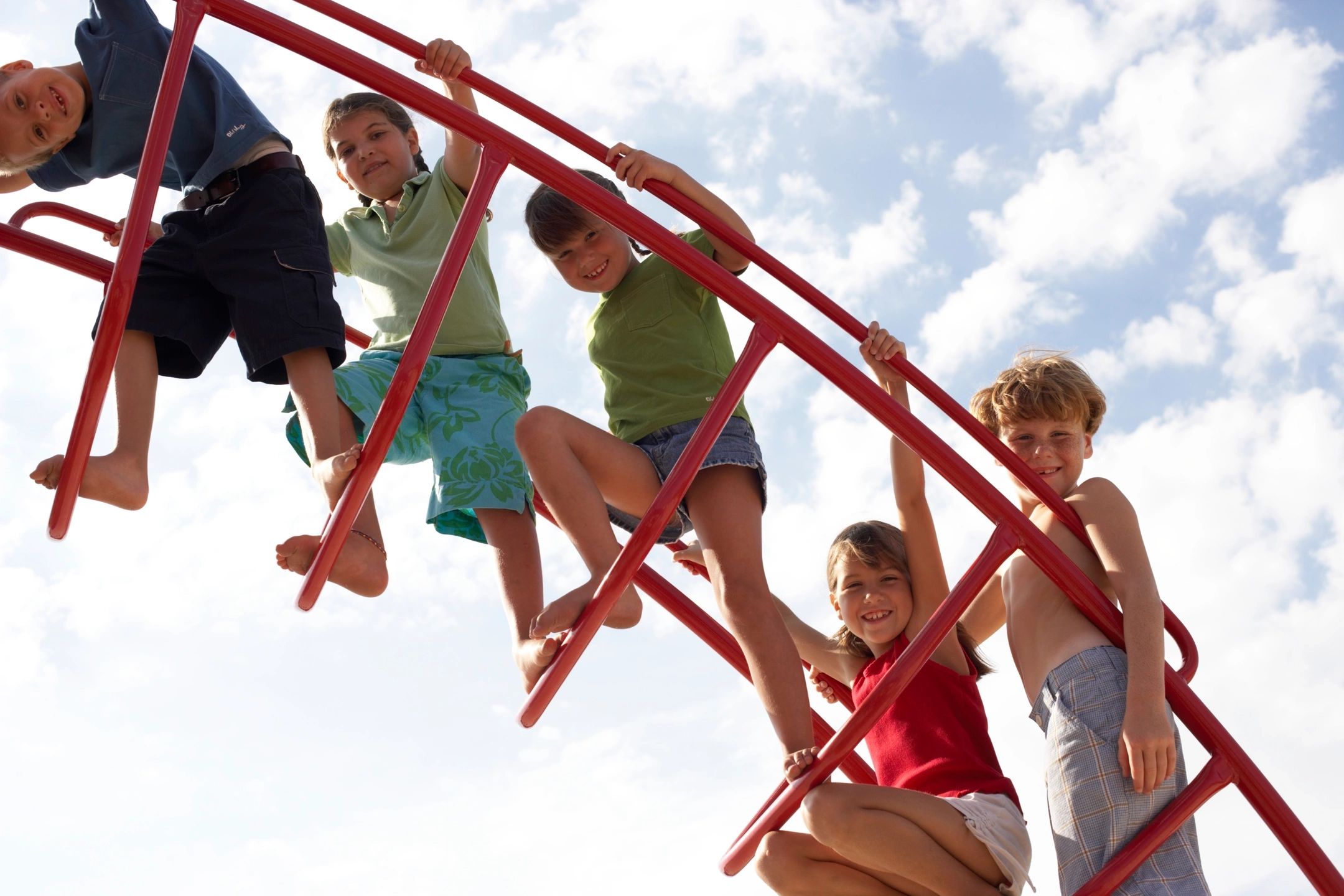 A group of kids hanging on to the side of a red slide.