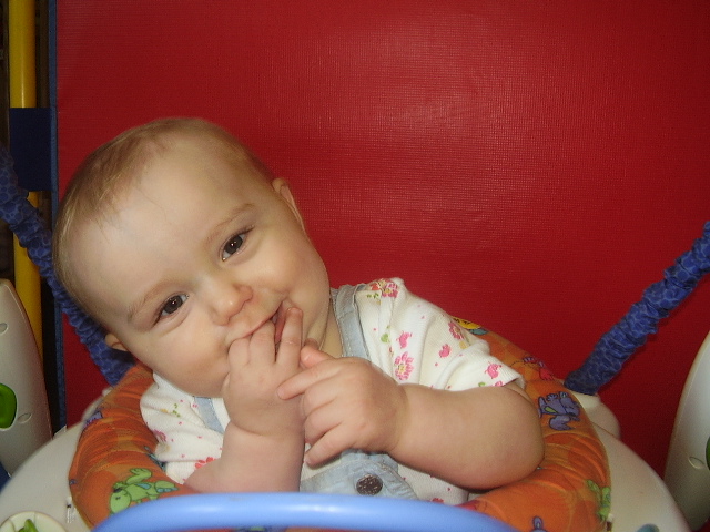 A baby sitting in a high chair with his hand under its chin.