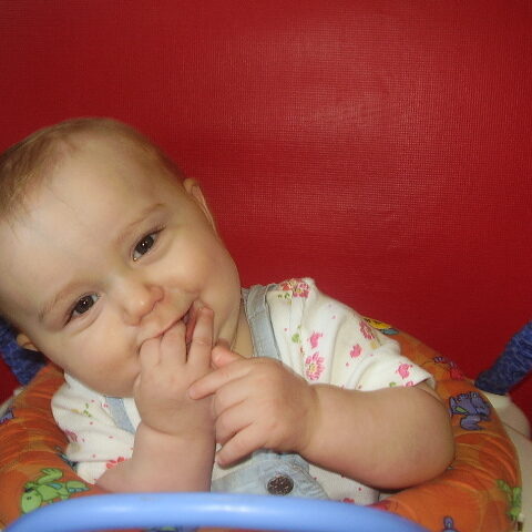A baby sitting in a high chair with his hand under its chin.